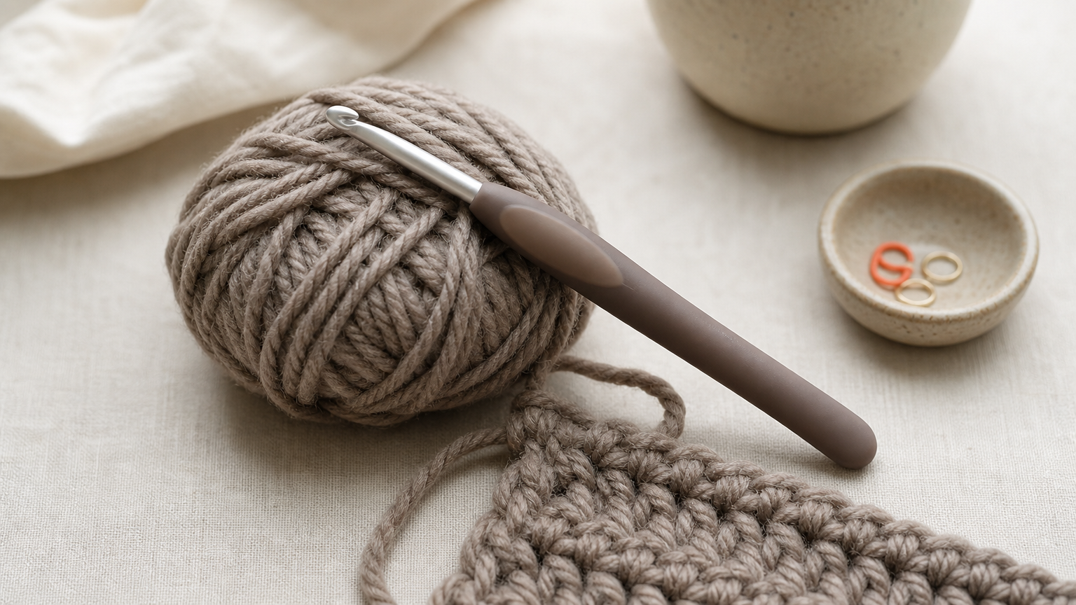 An ergonomic crochet hook with a cushioned grip lying beside a ball of yarn and a stitched swatch.