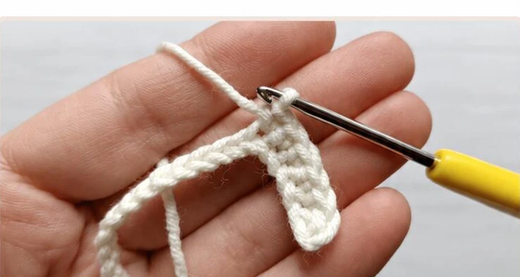 Cream crochet foundation stitches held on a yellow-handled hook