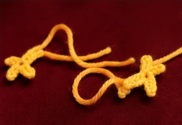 Two orange crocheted duck feet with three toes and long yarn tails
