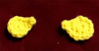 Two small yellow crocheted duck wings on a red background