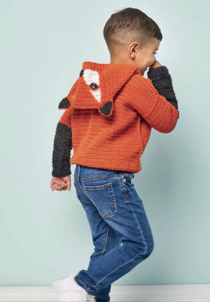 Child wearing the orange crochet fox hoodie with the fox-face hood resting on the back
