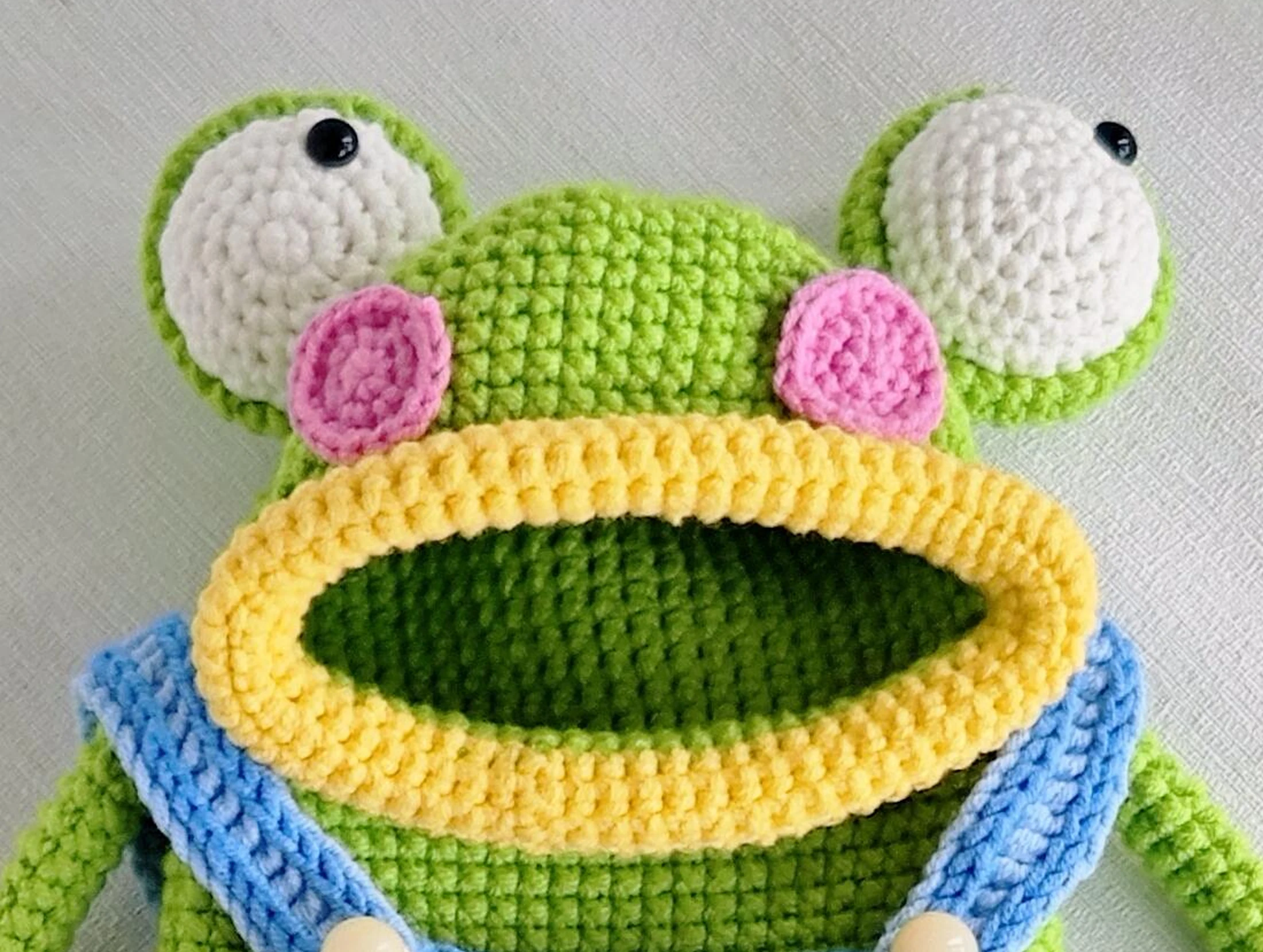 Raised white crochet frog eyes, pink cheeks and a thick yellow mouth edge