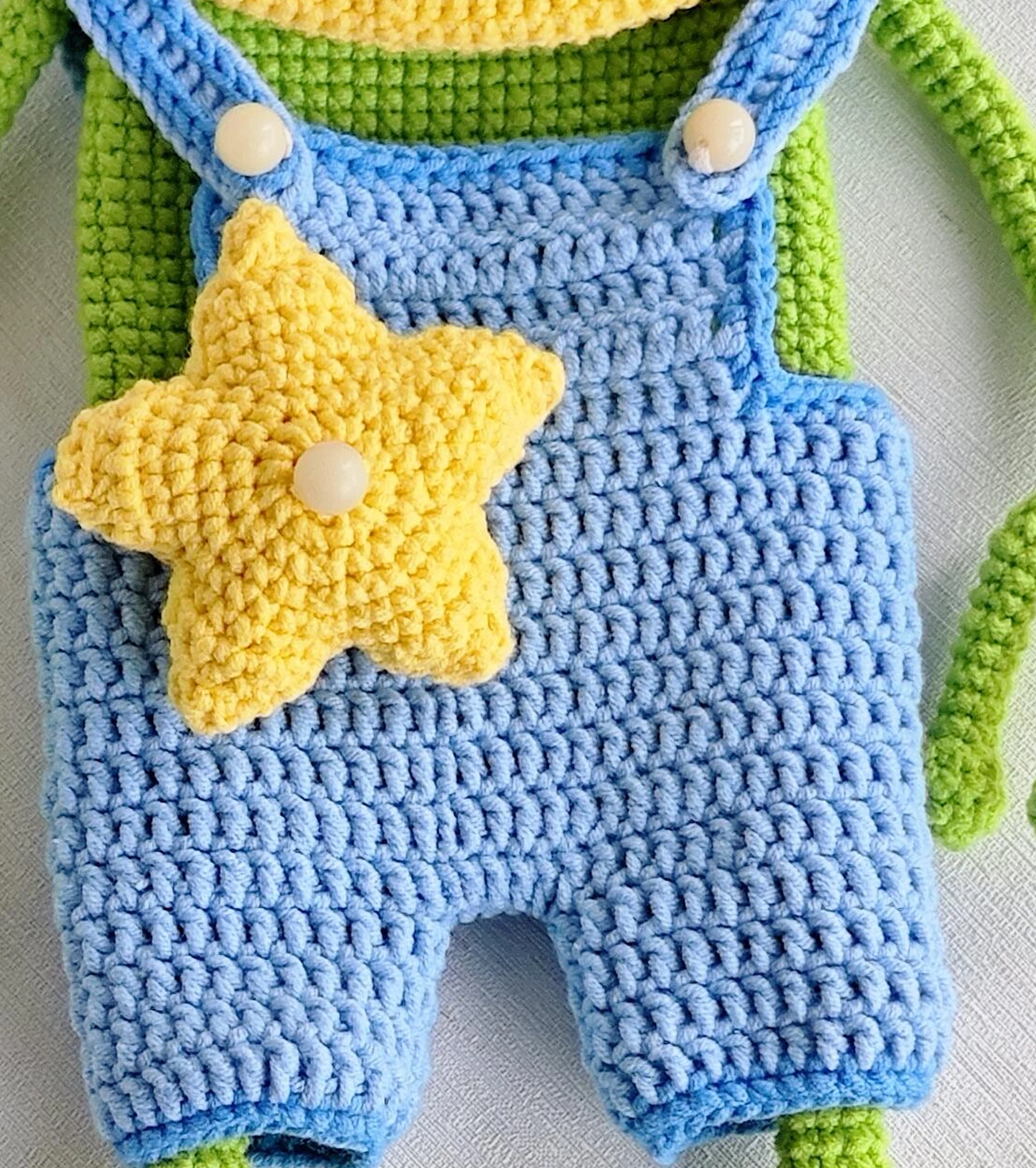 Blue crochet frog overalls with cream buttons and a yellow five-point star