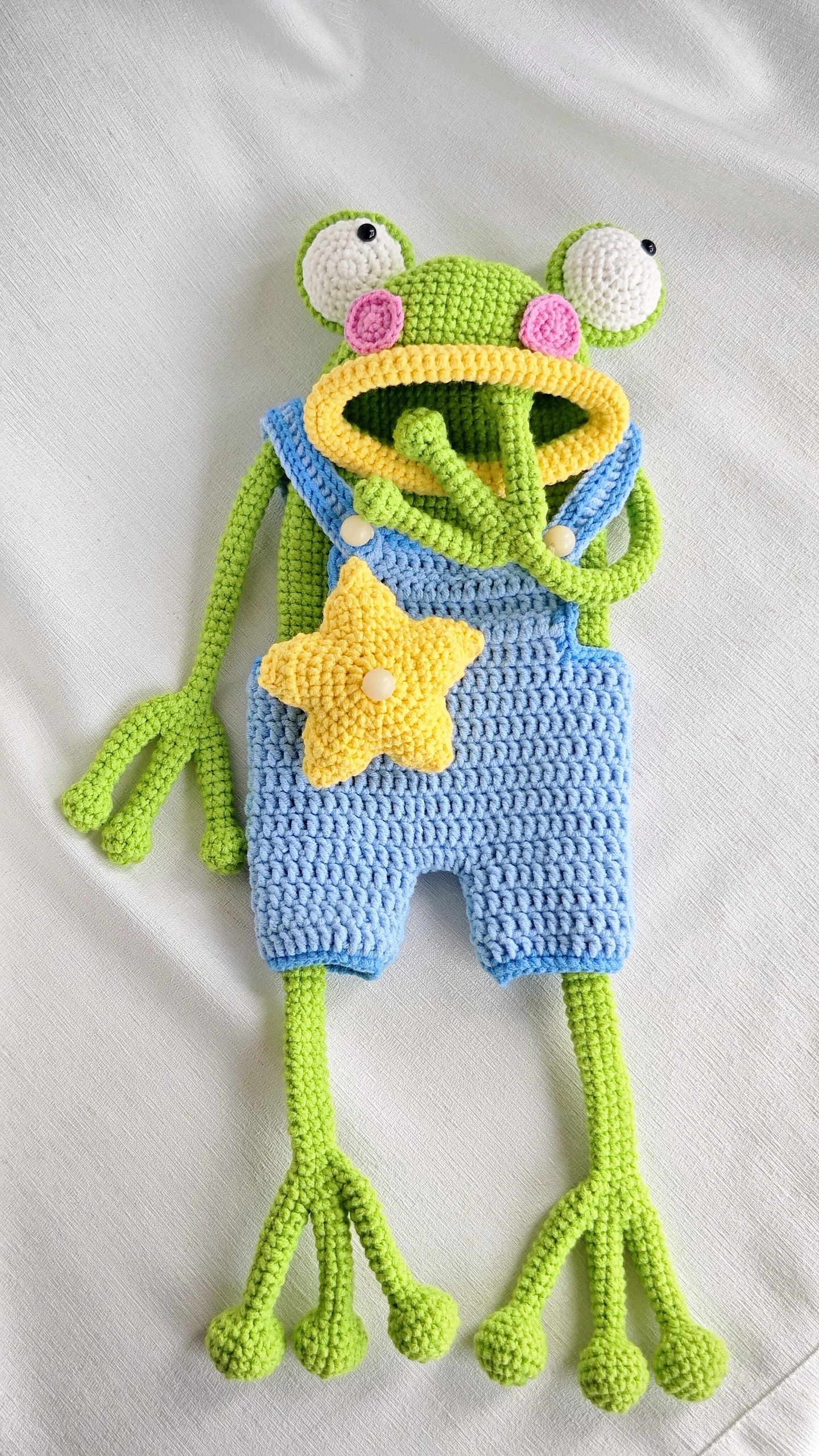 Green crochet frog bag with one hand raised across its yellow mouth