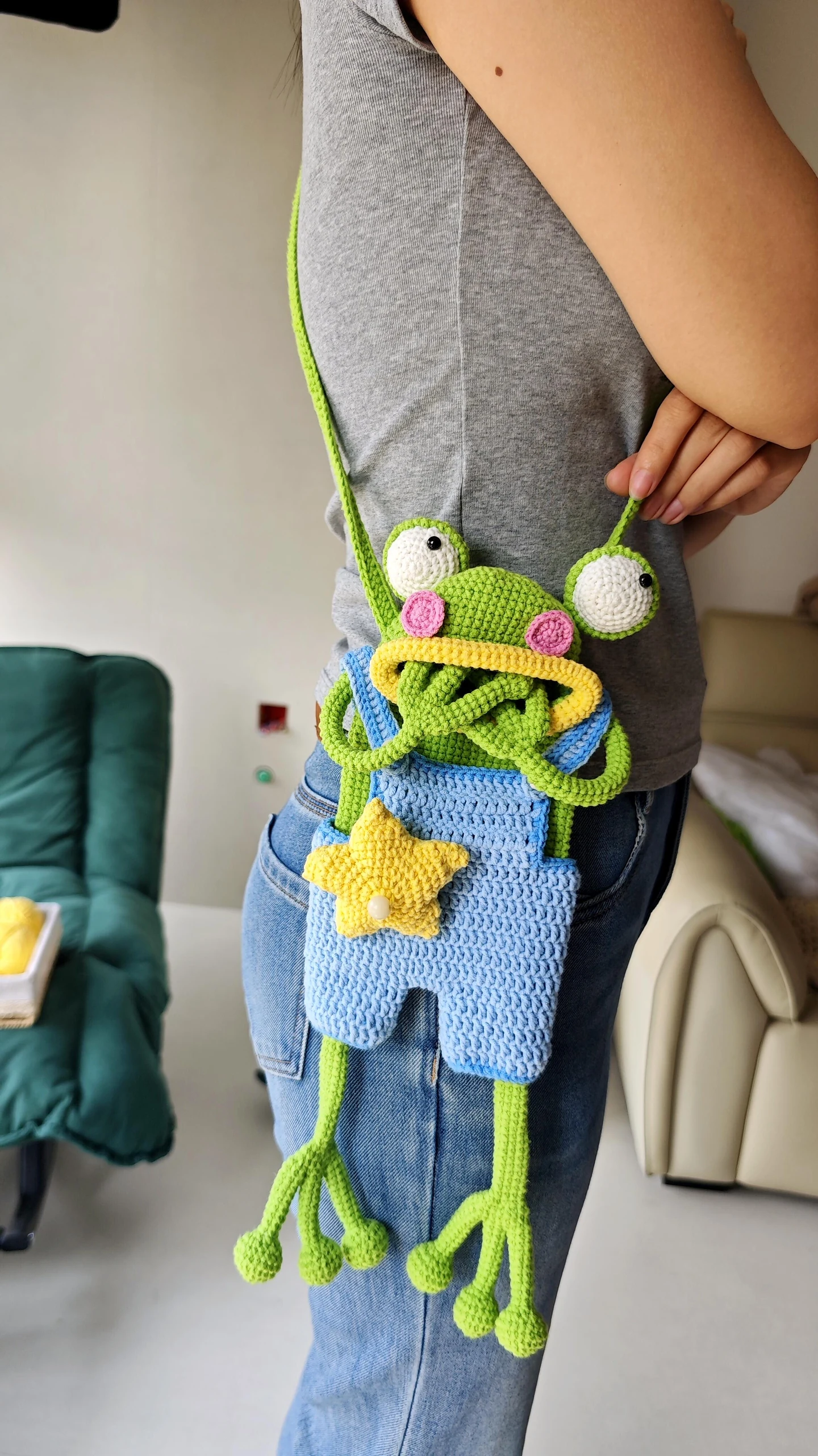 Crochet frog shoulder bag worn at the hip on a long green strap