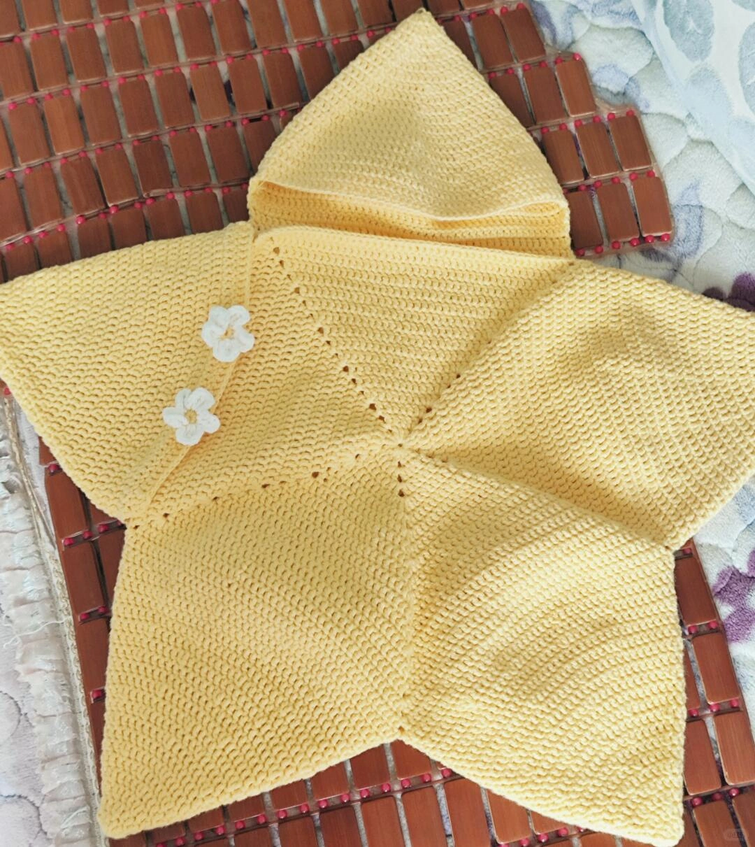 Yellow crochet star wrap with two white flower decorations before the final hood trim