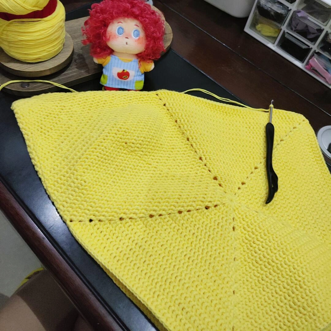 Yellow five-sector crochet panel laid flat beside the working hook