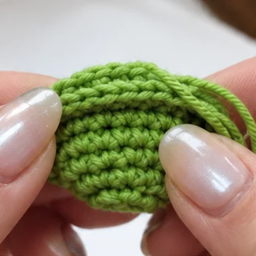 Hands shaping the green circular mouth piece for a long-neck crochet frog
