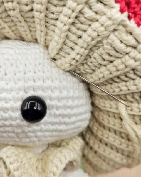 Cap sewing close-up: the needle joins the beige underside to the upper head fabric.