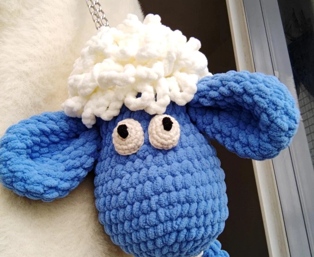 Blue crocheted sheep face with broad floppy ears and white curled fleece