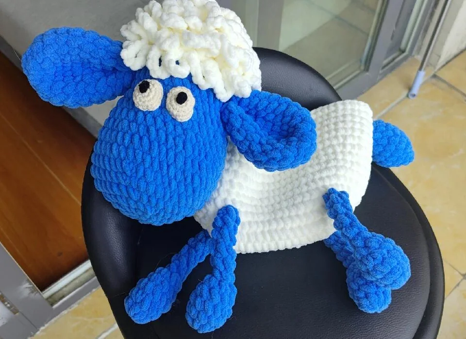 Plush sheep crochet bag laid flat with blue limbs and a white oval pouch